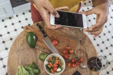 Nahaufnahme einer Frau in der Küche, die eine gesunde Mahlzeit zubereitet und ein Smartphone hält - VPIF01980