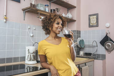 Smiling young woman drinking glass of red wine in kitchen - VPIF01984