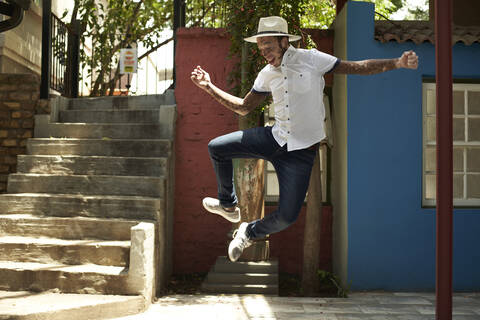 Portrait of young man with vitiligo wearing a hat, jumping in the street stock photo