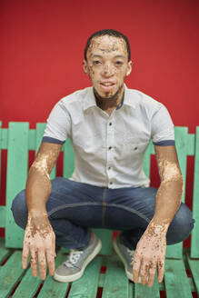 Young man with vitiligo on a green bench in front of a red wall - VEGF01358