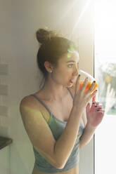 Female teenager drinking juice and looking out of the window - JPTF00400