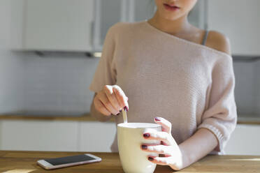 Weiblicher Teenager mit Tasse und Smartphone in der Küche - JPTF00410