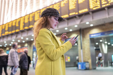 Woman at train station checking her smartphone - WPEF02432