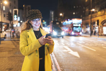 Frau mit ihrem Smartphone in der Stadt bei Nacht neben einer Straße - WPEF02439