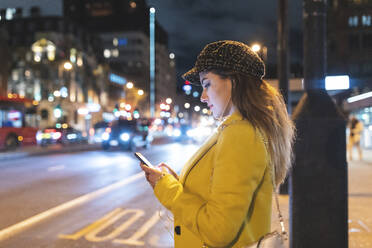 Frau mit ihrem Smartphone in der Stadt bei Nacht neben einer Straße in London, Großbritannien - WPEF02443