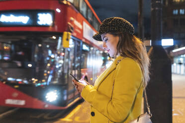 Glückliche Frau wartet auf den Bus in der Stadt bei Nacht, London, Großbritannien - WPEF02444