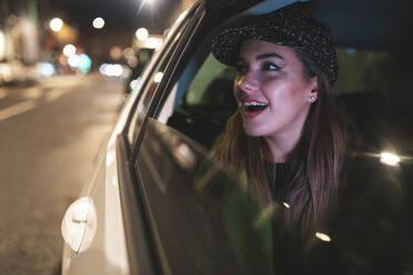 Frau sitzt auf der Rückbank eines Autos in der Stadt bei Nacht und schaut aus dem Autofenster - WPEF02448