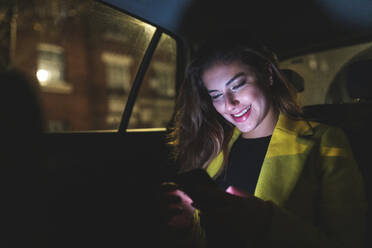 Frau auf dem Rücksitz eines Autos in der Stadt bei Nacht - WPEF02450