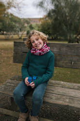 Porträt eines glücklichen Jungen mit Fernglas auf einer Bank im Herbst - GRCF00034