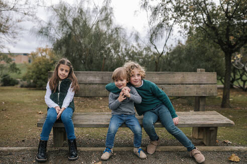 Gruppenbild von drei Kindern, die auf einer Holzbank im Freien sitzen - GRCF00037