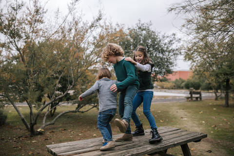 Drei Kinder tanzen auf Picknicktisch im Herbst und haben Spaß, lizenzfreies Stockfoto