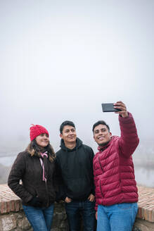 Junge mexikanische Freunde machen ein Selfie an einem nebligen Tag, Toledo, Spanien - GRCF00049