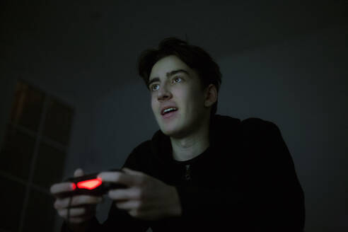 Teenage boy playing video game with console in the dark - AJOF00077