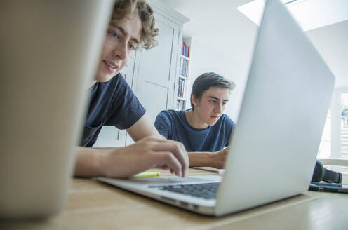 Two teenage boys using laptop and tablet on table at home - AJOF00079