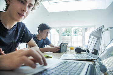 Zwei Teenager benutzen Laptop und Tablet auf dem Tisch zu Hause - AJOF00082