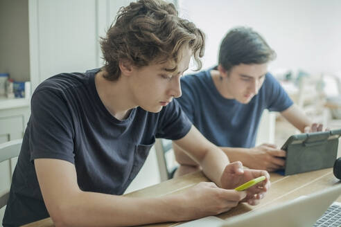 Zwei Jungen im Teenageralter benutzen Smartphone und Tablet auf dem Tisch zu Hause - AJOF00086