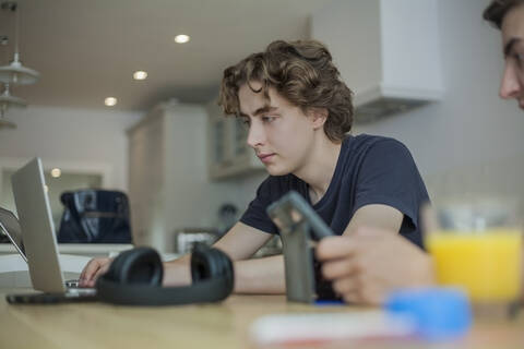 Zwei Jungen im Teenageralter benutzen Smartphone und Laptop auf dem Tisch zu Hause, lizenzfreies Stockfoto