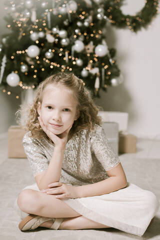 Porträt eines blonden kleinen Mädchens, das vor einem Weihnachtsbaum sitzt, lizenzfreies Stockfoto