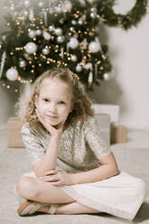 Porträt eines blonden kleinen Mädchens, das vor einem Weihnachtsbaum sitzt - EYAF00803
