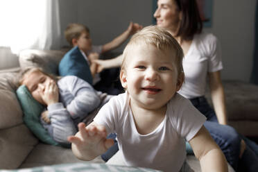 Porträt eines glücklichen kleinen Jungen mit seiner Familie auf der Couch im Wohnzimmer zu Hause - KMKF01157