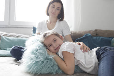 Porträt eines lächelnden Mädchens mit ihrer Mutter auf der Couch im Wohnzimmer zu Hause - KMKF01161