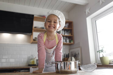Portrait of smiling girl wearing chef's hat in the kitchen - KMKF01164