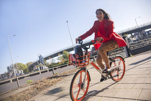 Junge Frau fährt mit einem Leihfahrrad durch die Stadt - AJOF00095