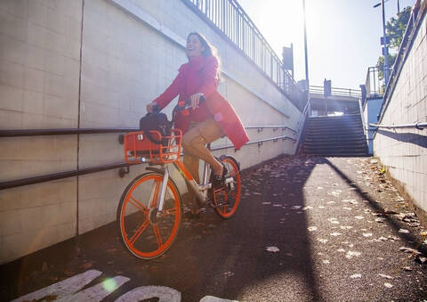 Junge Frau fährt mit einem Leihfahrrad durch die Stadt, lizenzfreies Stockfoto