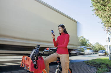 Young woman sitting on rental bike, using smartphone - AJOF00106