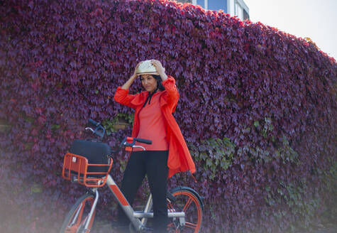 Junge Frau sitzt auf einem Fahrrad und setzt einen Sicherheitshelm auf - AJOF00110