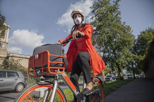 Junge Frau mit Helm und Gesichtsmaske, Fahrradfahren in der Stadt - AJOF00114