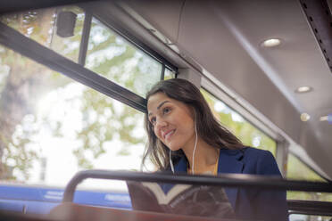 Young woman listening music on a bus with earphones, looking out of window - AJOF00122