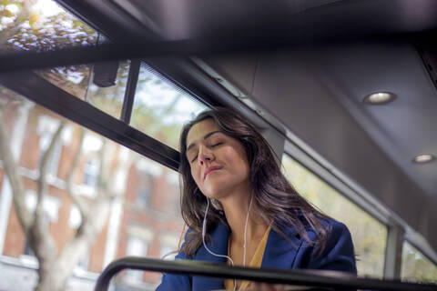 Junge Frau hört Musik in einem Bus mit Kopfhörern, Augen geschlossen, lizenzfreies Stockfoto