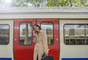 Young businesswoman using smartphone infront of commuter train - AJOF00125