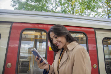 Junge Geschäftsfrau mit Smartphone vor einem Nahverkehrszug - AJOF00126