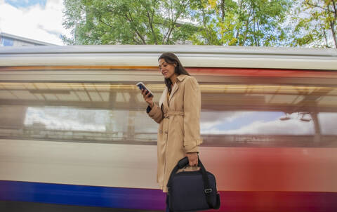 Junge Geschäftsfrau mit Smartphone vor einem Nahverkehrszug, lizenzfreies Stockfoto