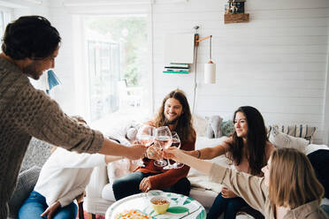 Male and female friends toasting wineglasses over food at table in cottage - MASF16099