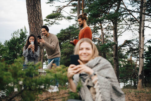 Männliche und weibliche Freunde benutzen Smartphones, während sie sich im Wald ausruhen - MASF16133