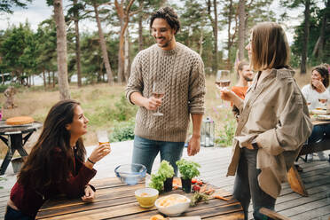 Smiling friends enjoying drinks while talking during garden party in yard - MASF16145