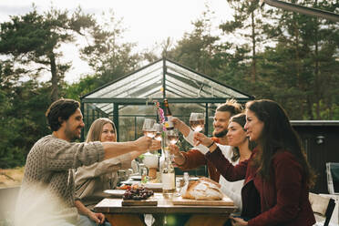 Male and female friends toasting wineglasses while enjoying dinner at garden party - MASF16151