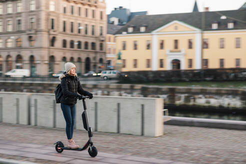 Full length of teenage girl riding e-scooter on street in city - MASF16158