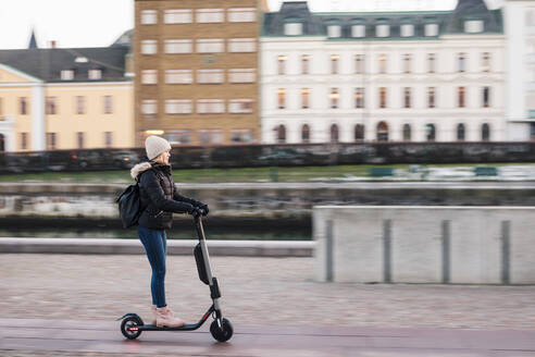 Side view of teenage girl riding electric push scooter on street in city - MASF16160