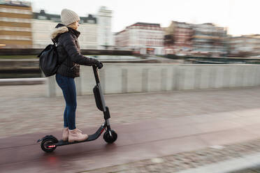 In voller Länge von Teenager-Mädchen Reiten elektrische Push-Roller auf der Straße in der Stadt im Winter - MASF16162