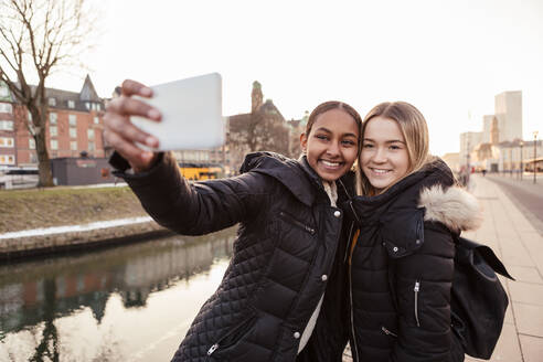 Teenager-Mädchen nimmt Selfie mit Freund auf Smartphone gegen Kanal in der Stadt - MASF16175