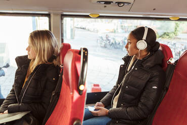 Teenager-Mädchen, das über Kopfhörer Musik hört, und Frau, die durch das Fenster schaut, während sie im Bus reist - MASF16181