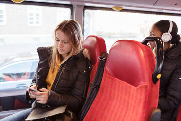 Teenager-Mädchen, das ein Smartphone benutzt und über Kopfhörer Musik hört, während sie im Bus unterwegs ist - MASF16185