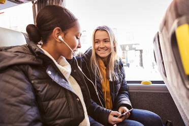 Glückliche Freunde hören gemeinsam Musik über Kopfhörer vom Smartphone im Bus - MASF16189