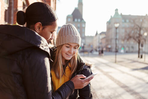 Teenager-Mädchen zeigt einem Freund in der Stadt sein Mobiltelefon - MASF16190