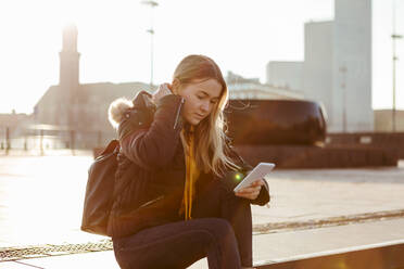 Teenager-Mädchen, das ein Smartphone benutzt, während es an einem sonnigen Tag auf einer Treppe sitzt - MASF16192