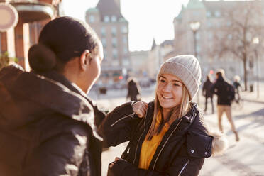 Smiling teenage girl talking to friend in city during winter - MASF16198